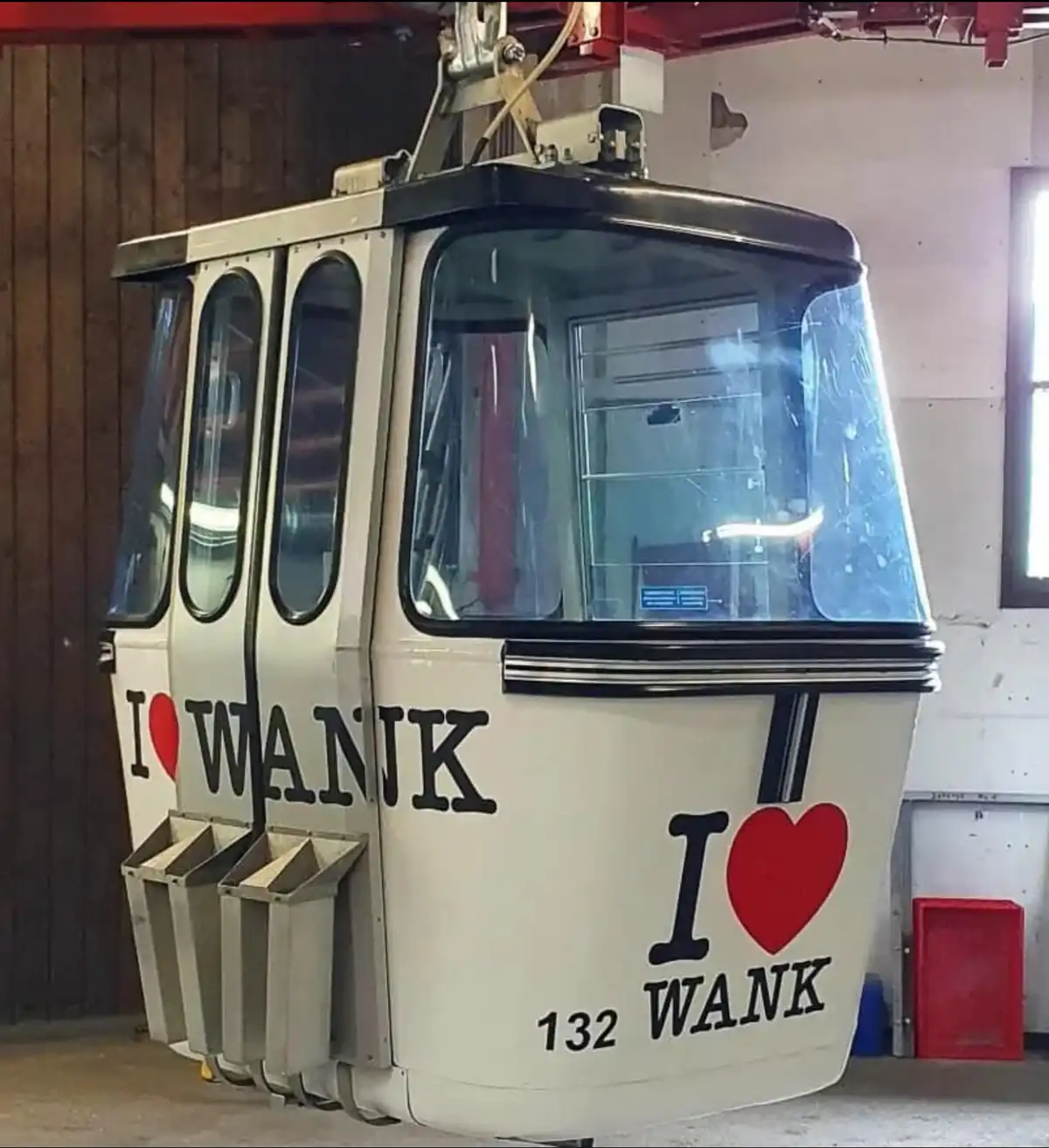 A white cable car, likely in a maintenance garage, has the phrase 'I ❤️ WANK' painted on its side in large black letters…