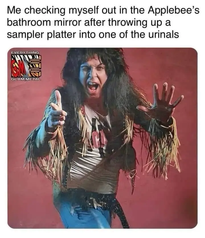 A man with long dark hair, wearing a fringed jacket and jeans, poses dramatically with one hand pointing and the other open…