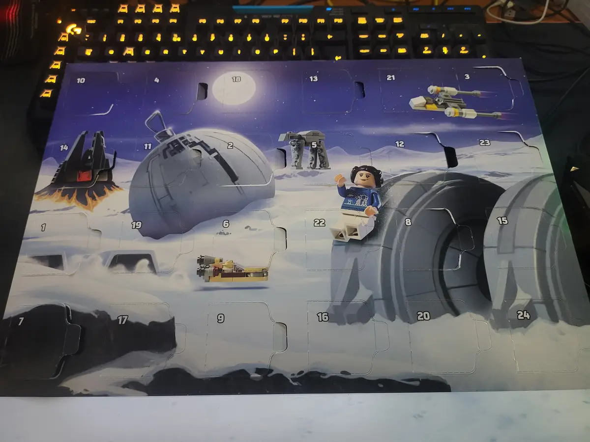 A Lego Star Wars Advent calendar with a snowy Hoth scene, featuring numbered flaps (1-24) with some opened to reveal mini…
