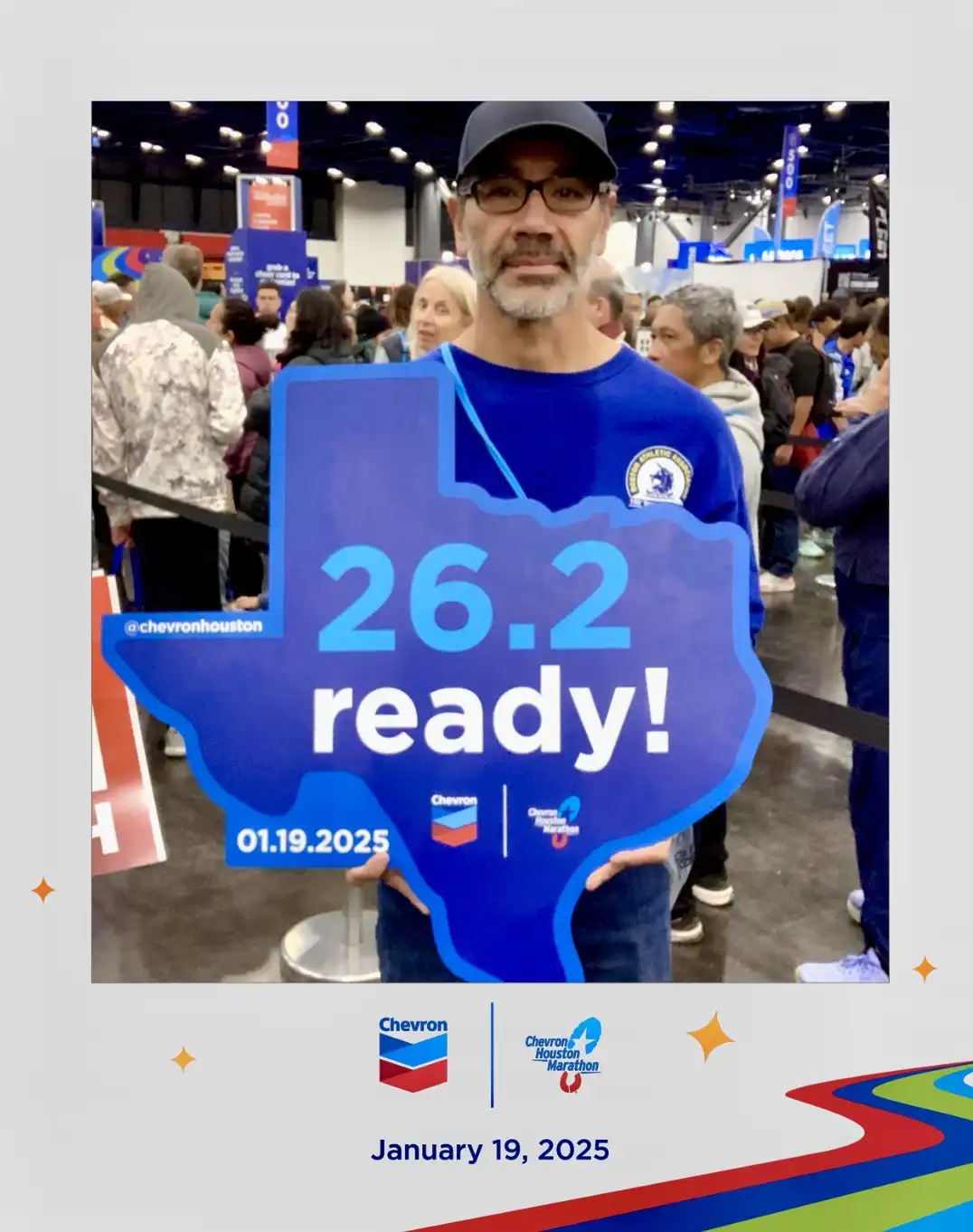 A man in a blue shirt and cap holds a large blue cutout shaped like the state of Texas. The cutout displays '26.2 ready!' in…