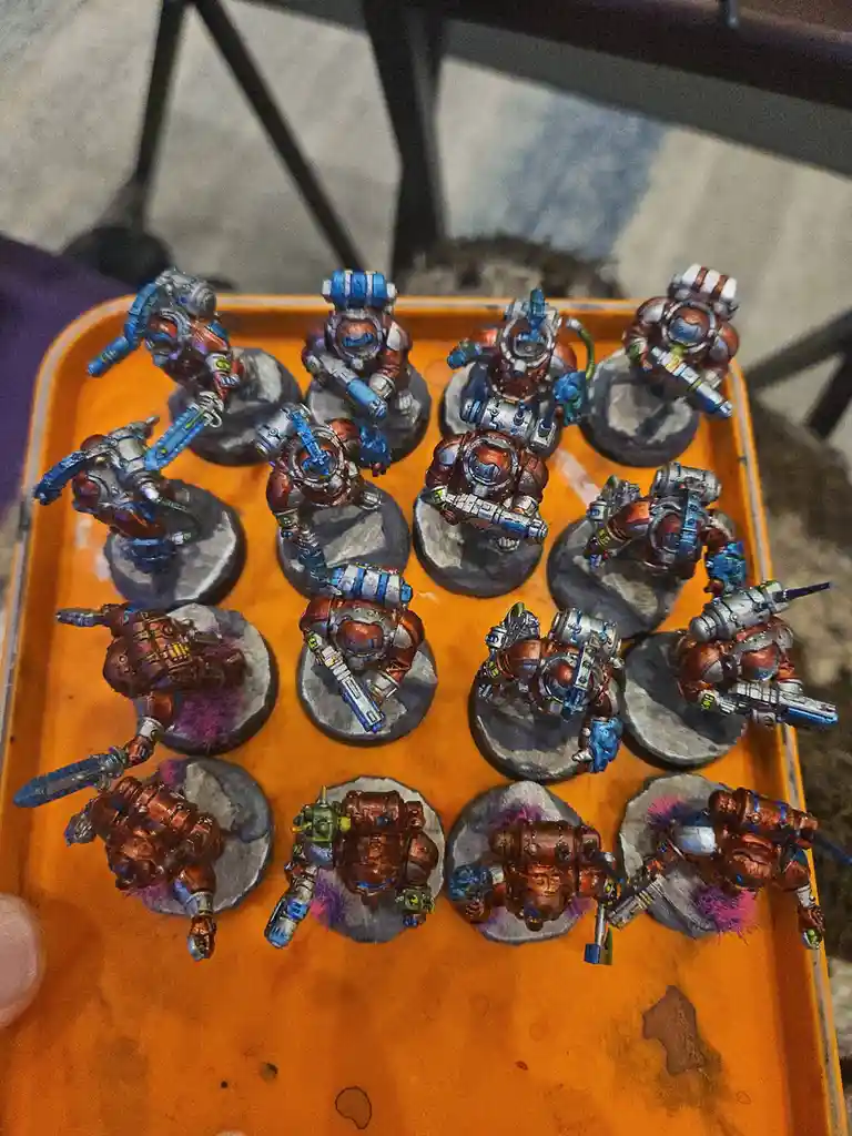 An orange tray holds twelve painted miniature figurines of armored warriors, each standing on a circular base. The…