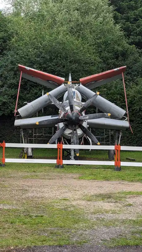 A vintage military aircraft, likely a de Havilland Mosquito, is displayed outdoors with its wings folded upward and…