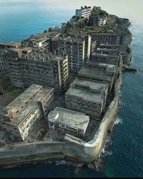 an aerial photograph shows a cluster of dilapidated, multi-story concrete buildings perched on a narrow, rocky peninsula…