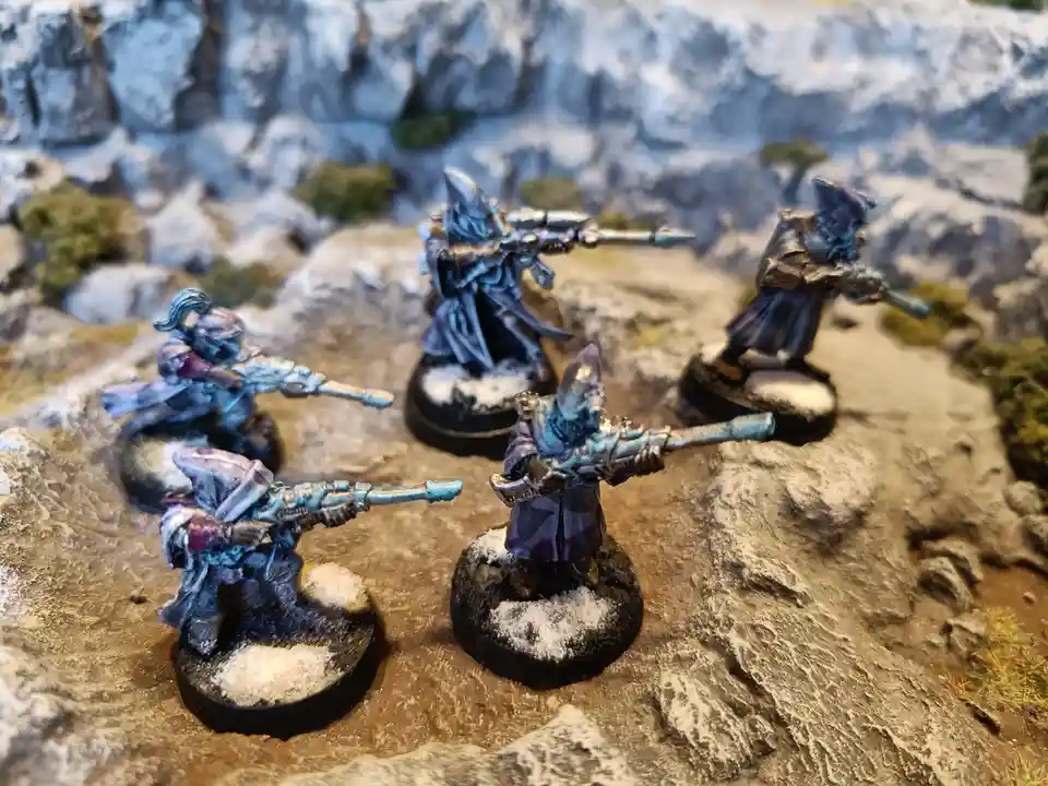 Five painted miniature fantasy figures, resembling wizards or sorcerers in dark robes and pointed hats, are posed on rocky…