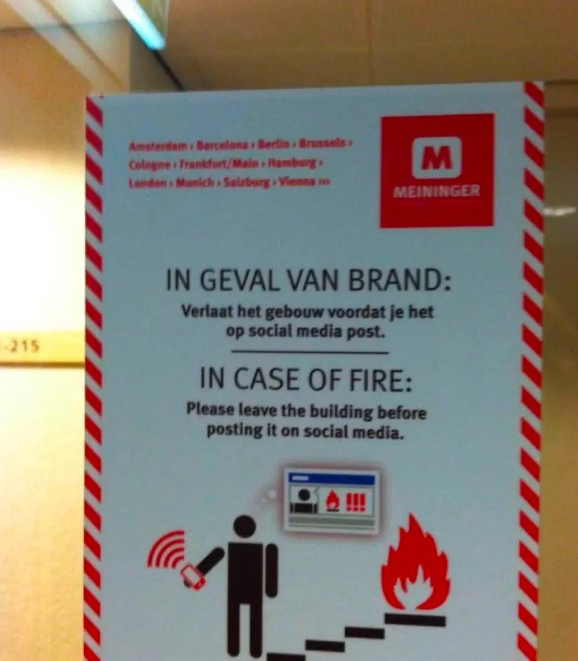 A fire safety sign from Meininger hotels, featuring Dutch and English text. It humorously instructs people to leave the…