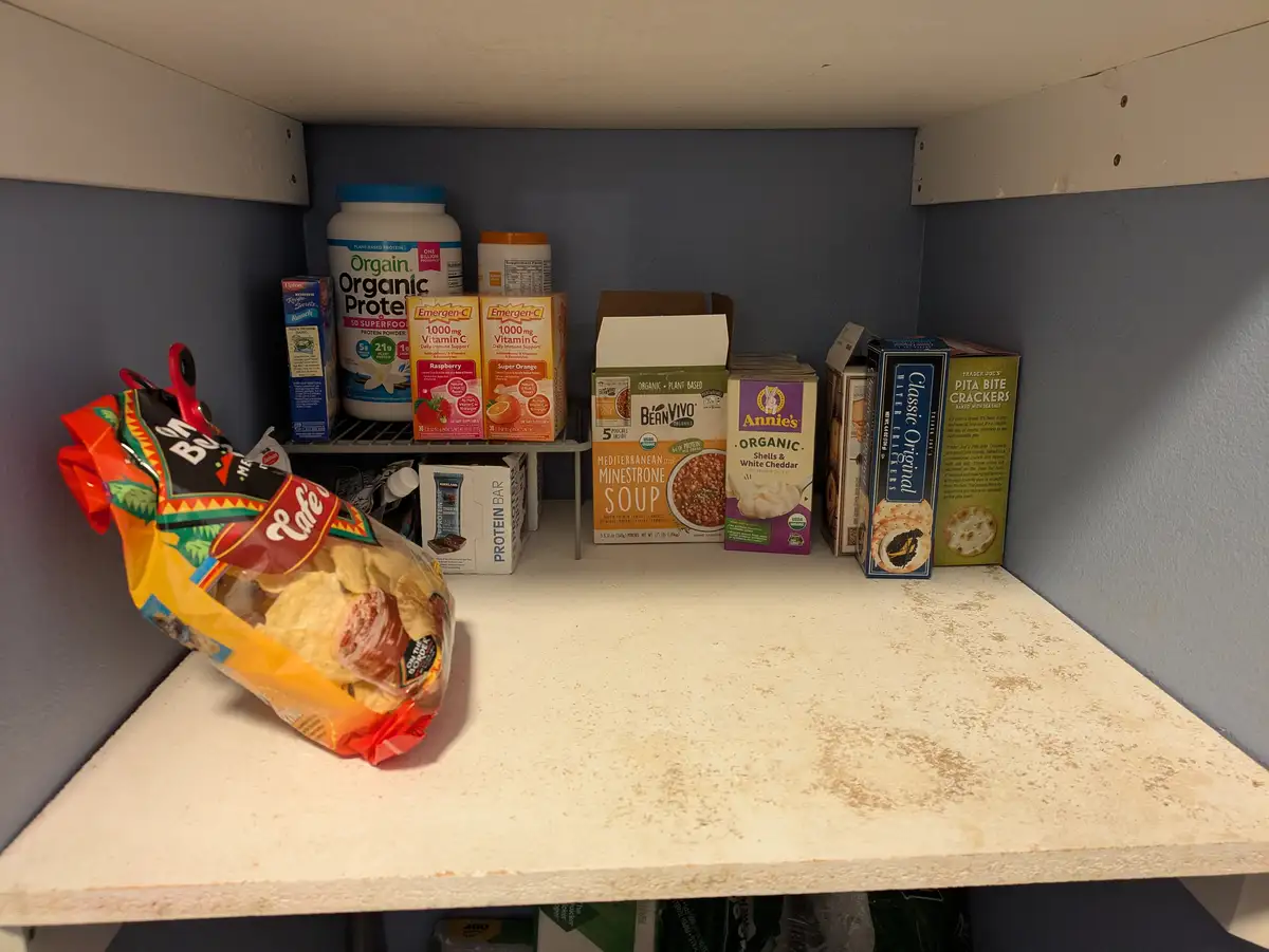 A pantry shelf displays an array of health-focused products like protein powder, vitamin C packets, organic soups, and…