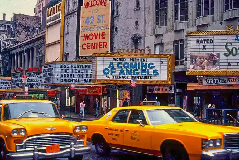 A vintage photo of a bustling New York City street with yellow taxis and movie theater marquees. One theater sign reads…