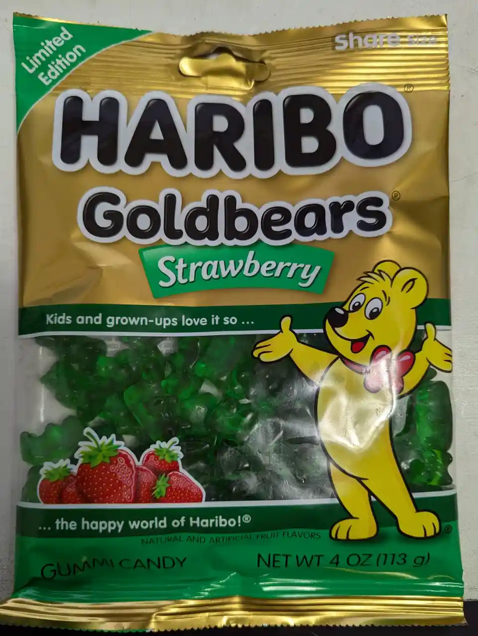 A close-up of a Haribo Goldbears Strawberry gummy candy bag, featuring green gummy bears visible through the clear window, a…