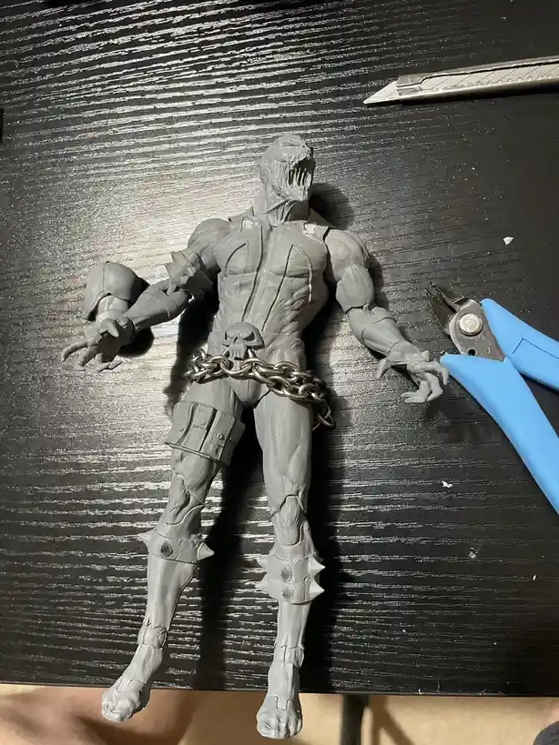A grey, unpainted action figure of a muscular, monstrous character with a screaming face and spiked boots lies on a black…