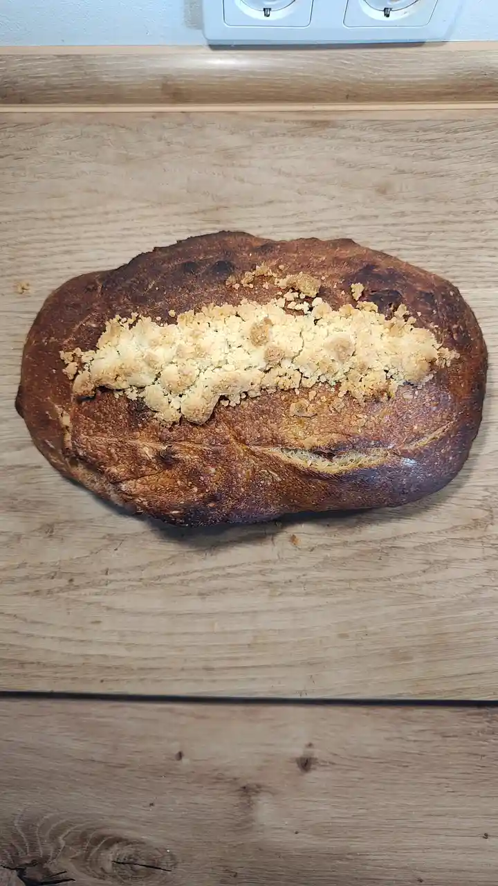 A rustic, oval-shaped loaf of bread with a dark, crusty exterior sits on a wooden surface. A generous, uneven layer of…