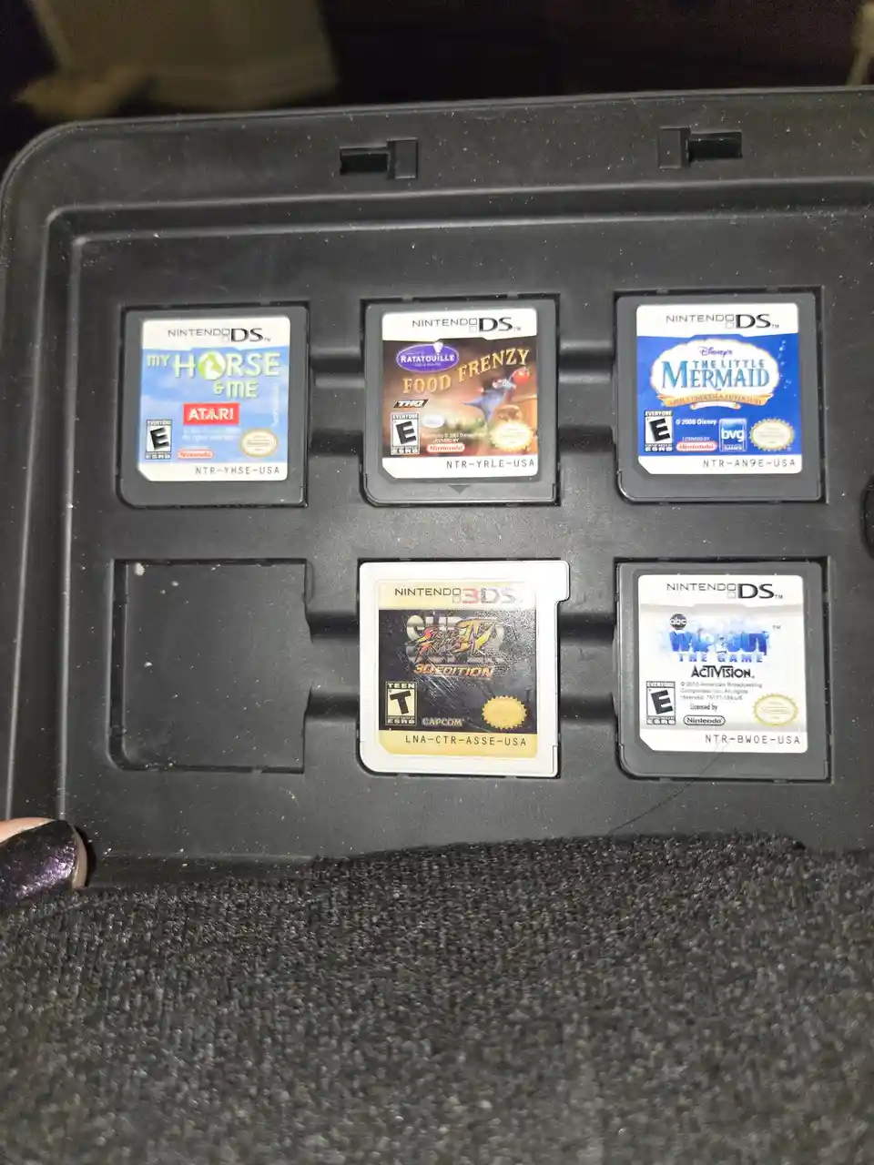 A close-up photo shows five Nintendo game cartridges in a black plastic case, with one slot empty. The visible cartridges…