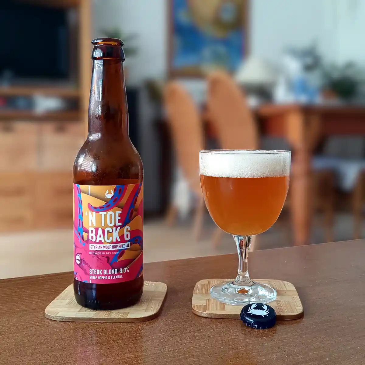 A brown beer bottle with a colorful label reading 'N TOE BACK 6' sits next to a glass of amber beer with a white head, both…