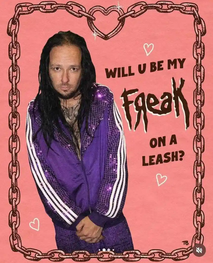 A man with long dark hair and a beard, wearing a sparkly purple tracksuit with white stripes, stands against a pink…