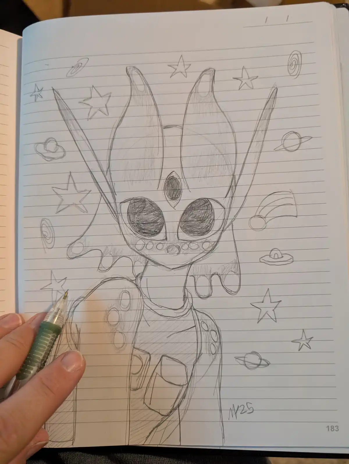 A hand-drawn pencil sketch on lined notebook paper shows a cartoonish alien creature with large eyes, spiky headgear, and a…