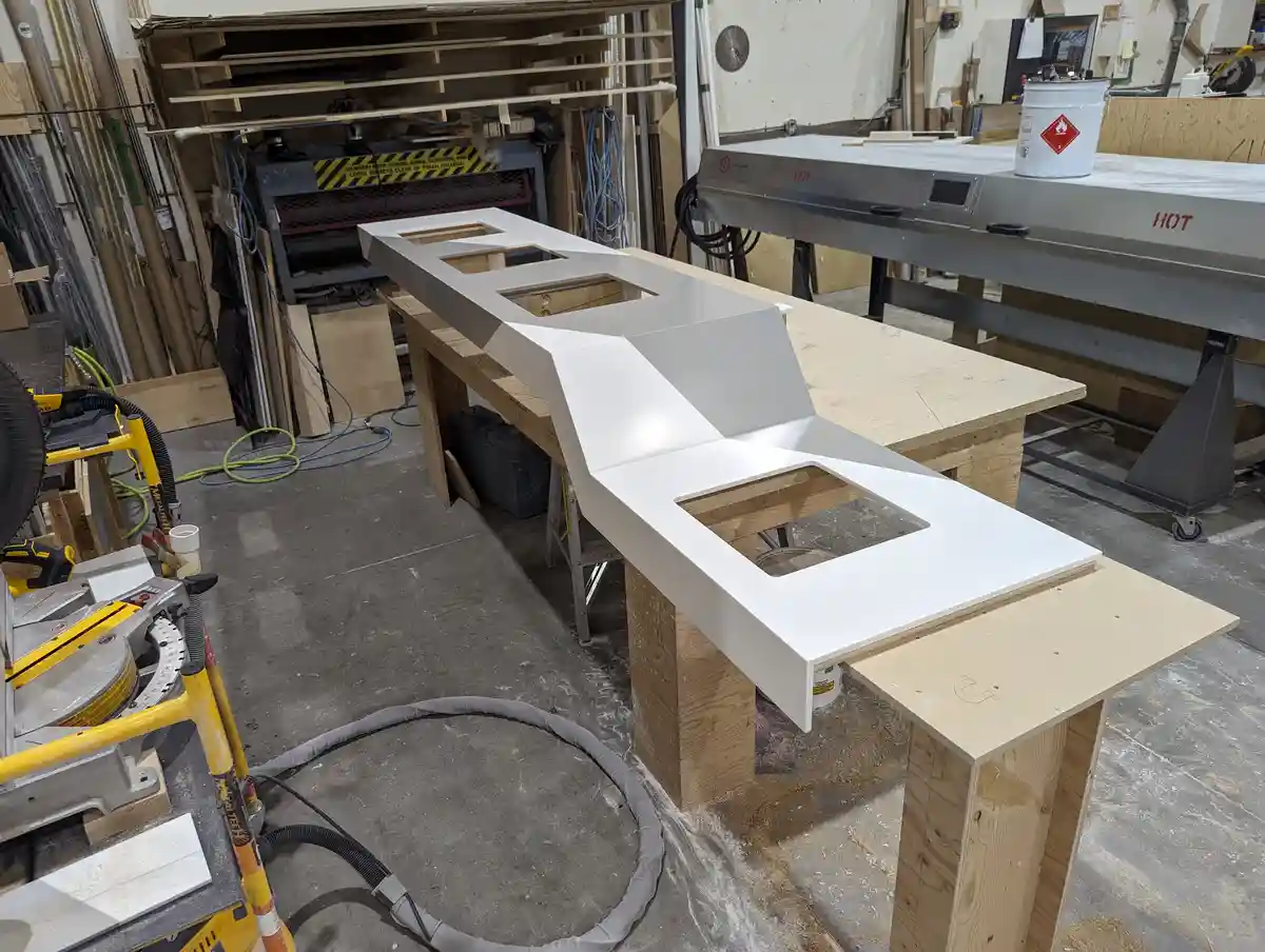 A white, angular, spaceship-shaped kitchen counter sits on wooden supports in a cluttered workshop filled with tools and…