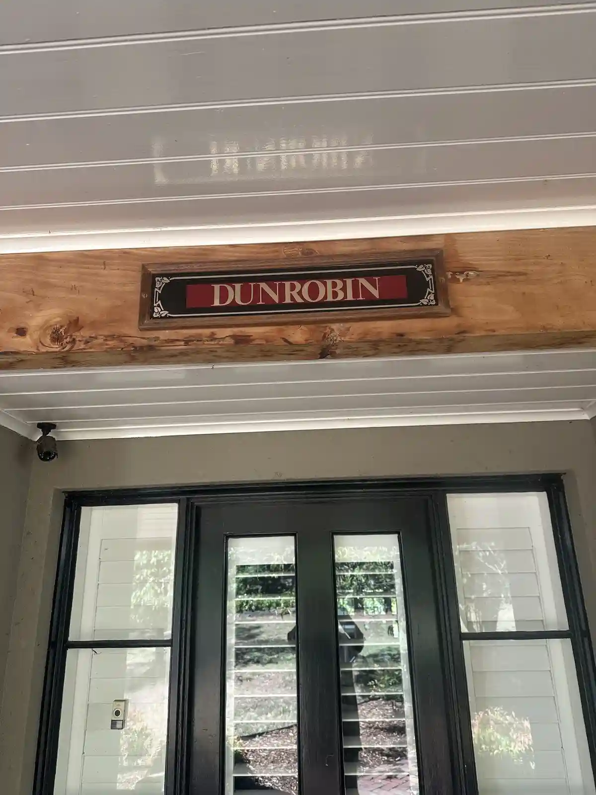 A close-up photo shows a wooden sign with the word 'DUNROBIN' in white capital letters on a red background, mounted above a…