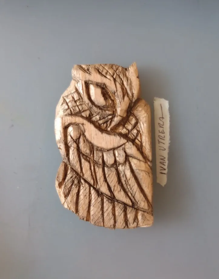 A carved wooden artifact, possibly a pendant or figurine, with abstract, angular lines etched into its surface, is displayed…
