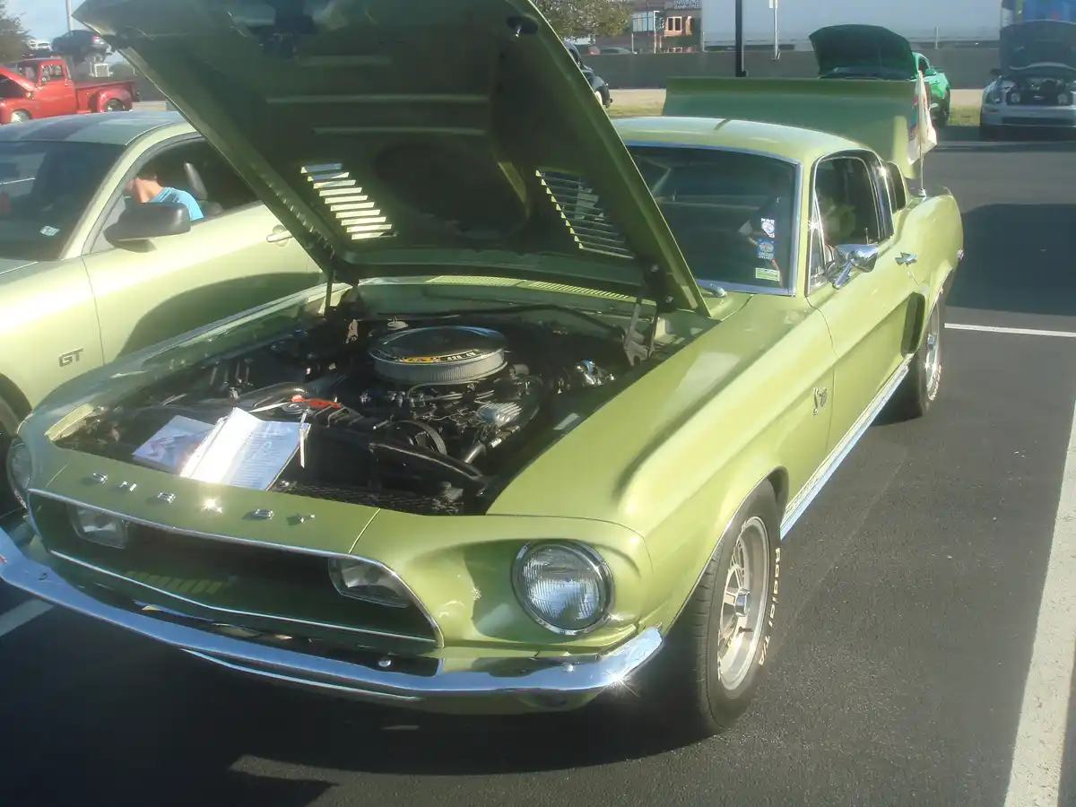 A lime-green classic Ford Mustang with its hood open, revealing a large engine with a visible '428 ci' label. The car is…