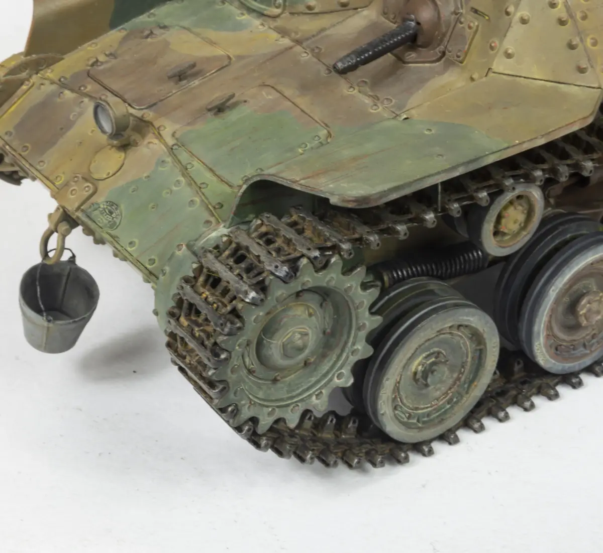 A close-up of a detailed, weathered model tank with green and tan camouflage, showing its tracks, wheels, and a small metal…