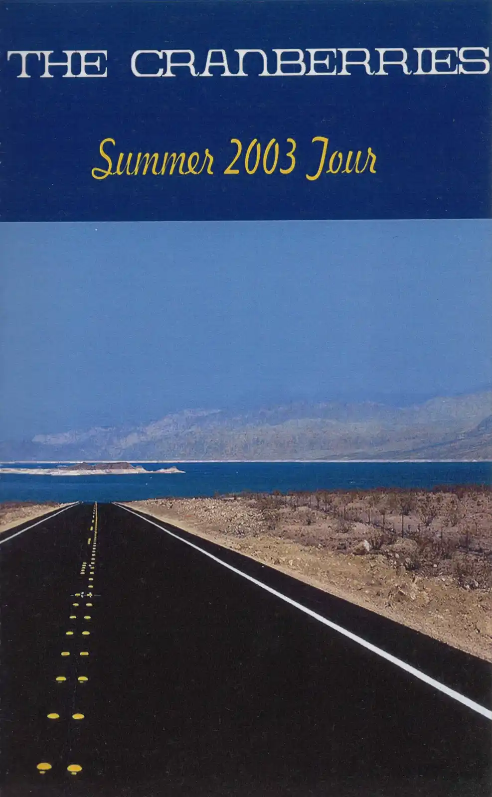 The image shows the cover of The Cranberries' Summer 2003 Tour program, featuring a long, straight road stretching toward a…