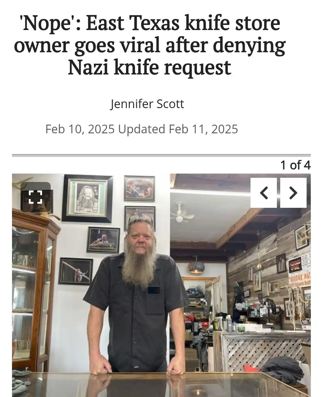 A man with a long gray beard and black shirt stands behind a glass counter in a knife shop, looking directly at the camera…