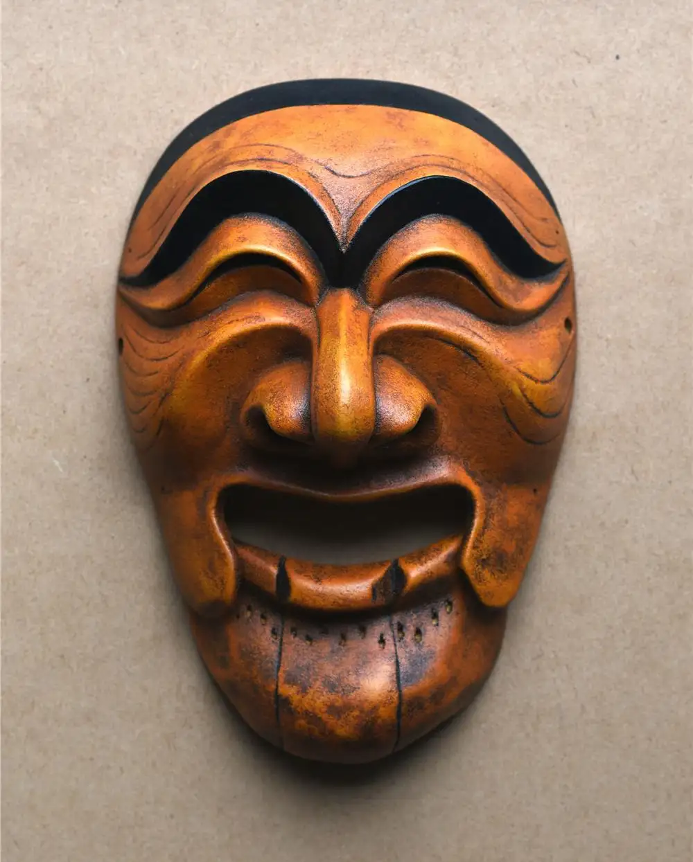 A close-up of a traditional Japanese wooden mask with exaggerated, joyful facial features, including wide, arched eyebrows…