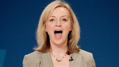 A woman with blonde hair and a beige blazer is shown with her mouth wide open in an expression of shock or disbelief, set…