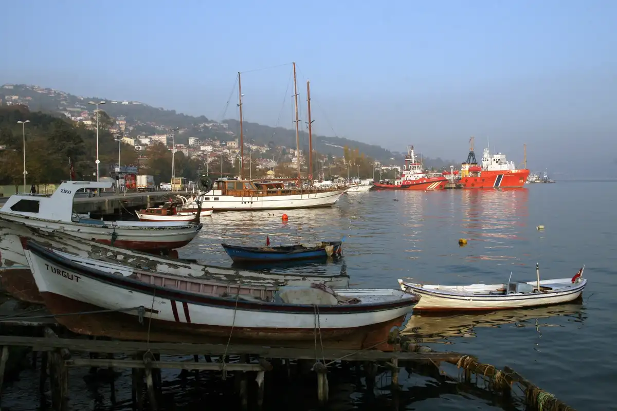 A scenic harbor photo shows small, weathered fishing boats in the foreground, some resting on wooden docks, with larger…