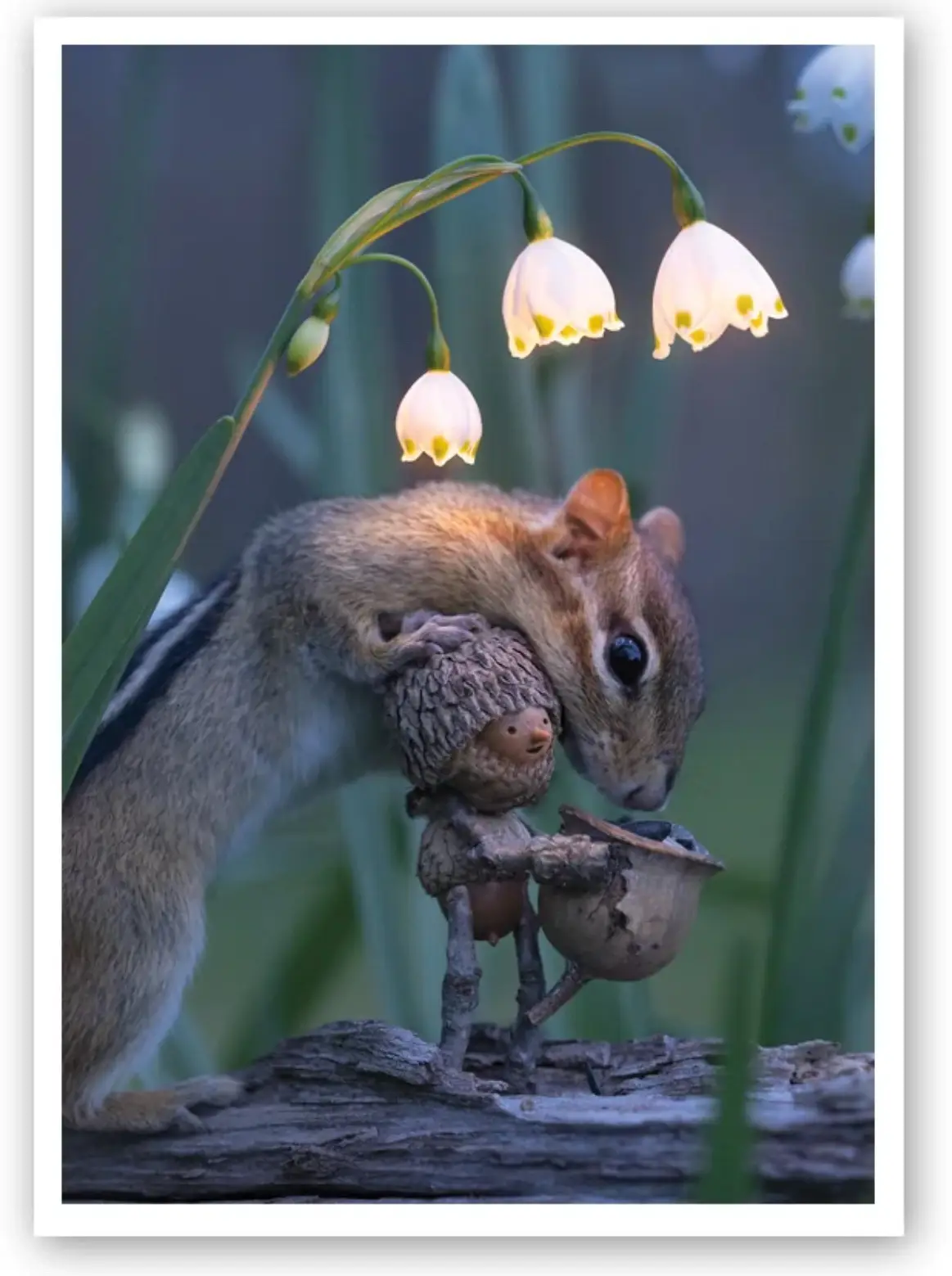 A chipmunk is shown holding a small, whimsical figurine made of acorns and twigs, which appears to be wearing a hat and…
