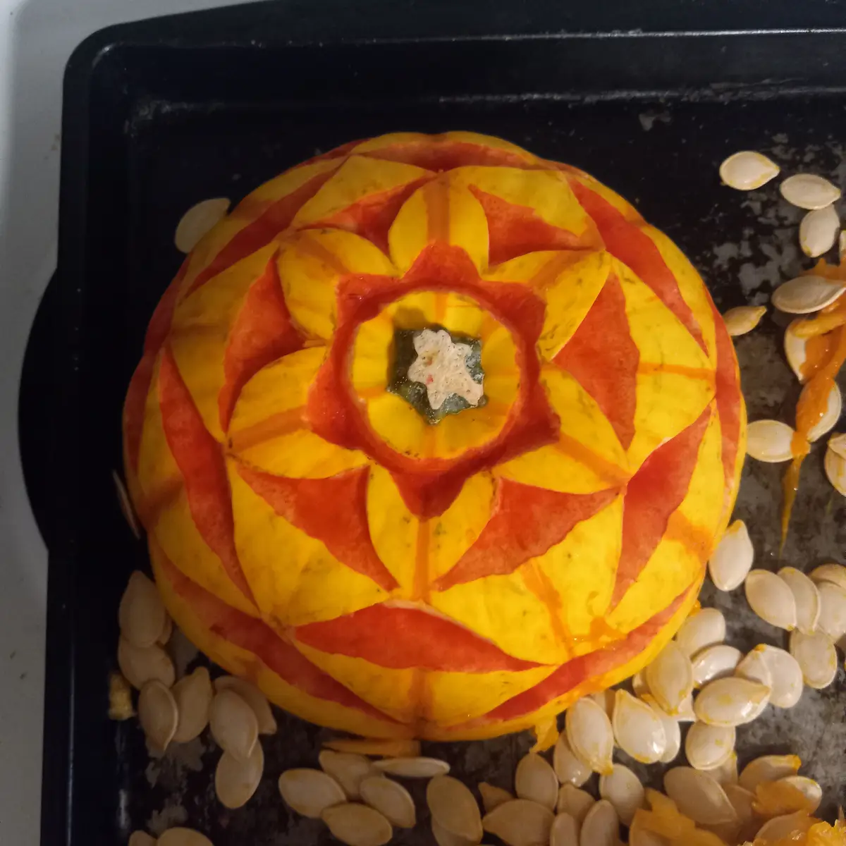 A top-down photo of a pumpkin with intricate, symmetrical orange and yellow carved patterns resembling a flower or mandala…