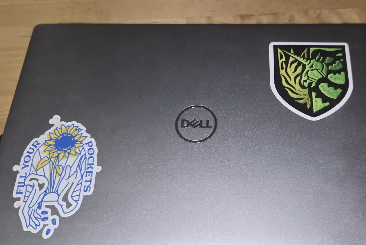 A black Dell laptop lid shows two stickers: one on the left features a sunflower and hands with the text 'FILL YOUR…