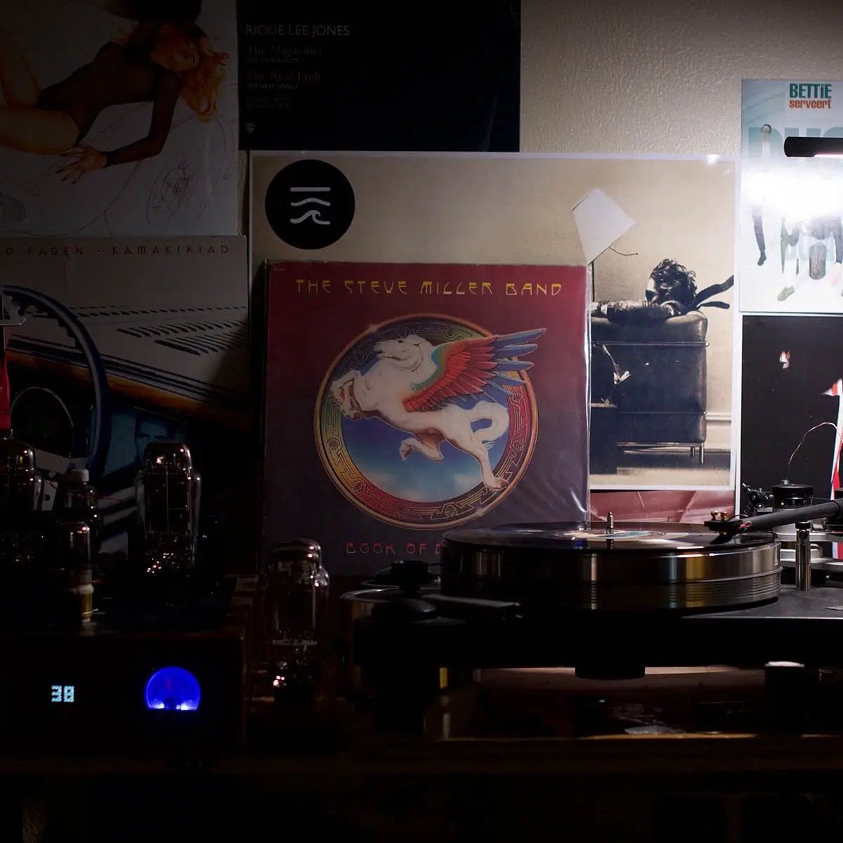 A dimly lit vinyl record setup features a turntable with a record spinning, surrounded by various album covers including…