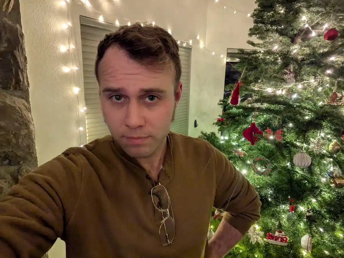 A man in a brown shirt with glasses hanging from his collar stares directly at the camera with a skeptical, unimpressed…