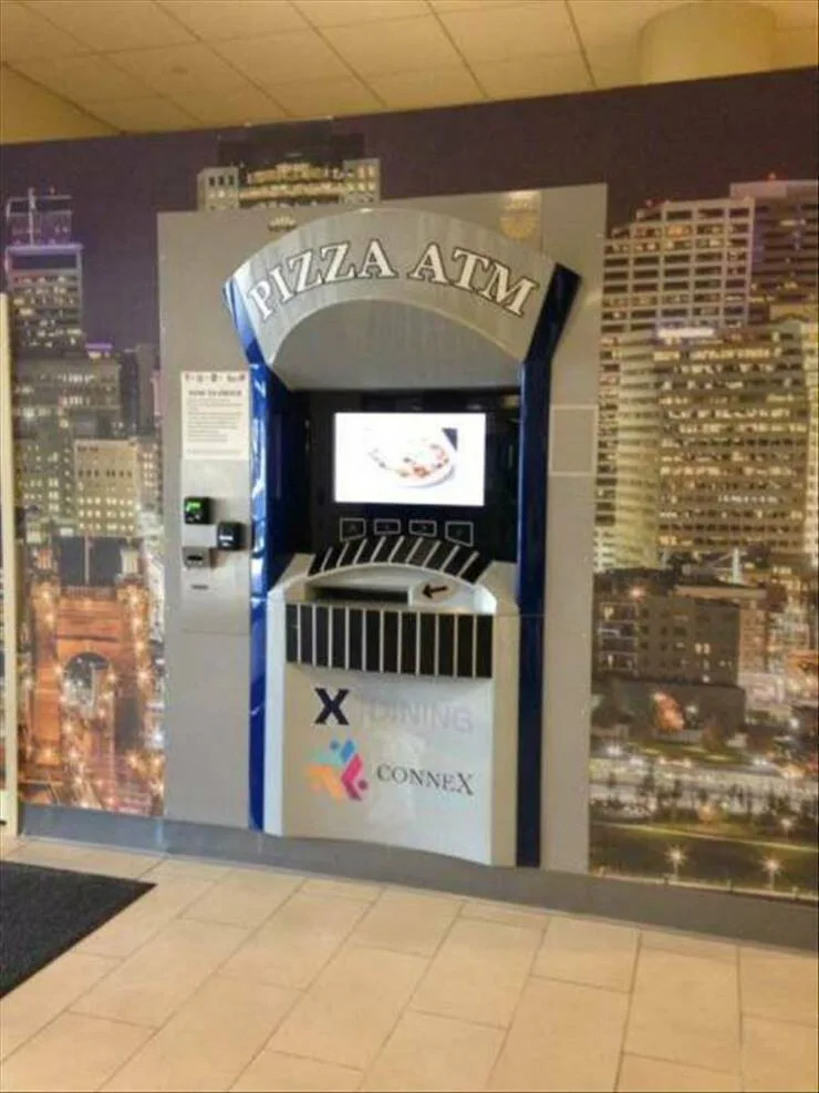 A large, silver and blue kiosk labeled 'PIZZA ATM' stands in a tiled lobby with a cityscape mural behind it. The machine has…
