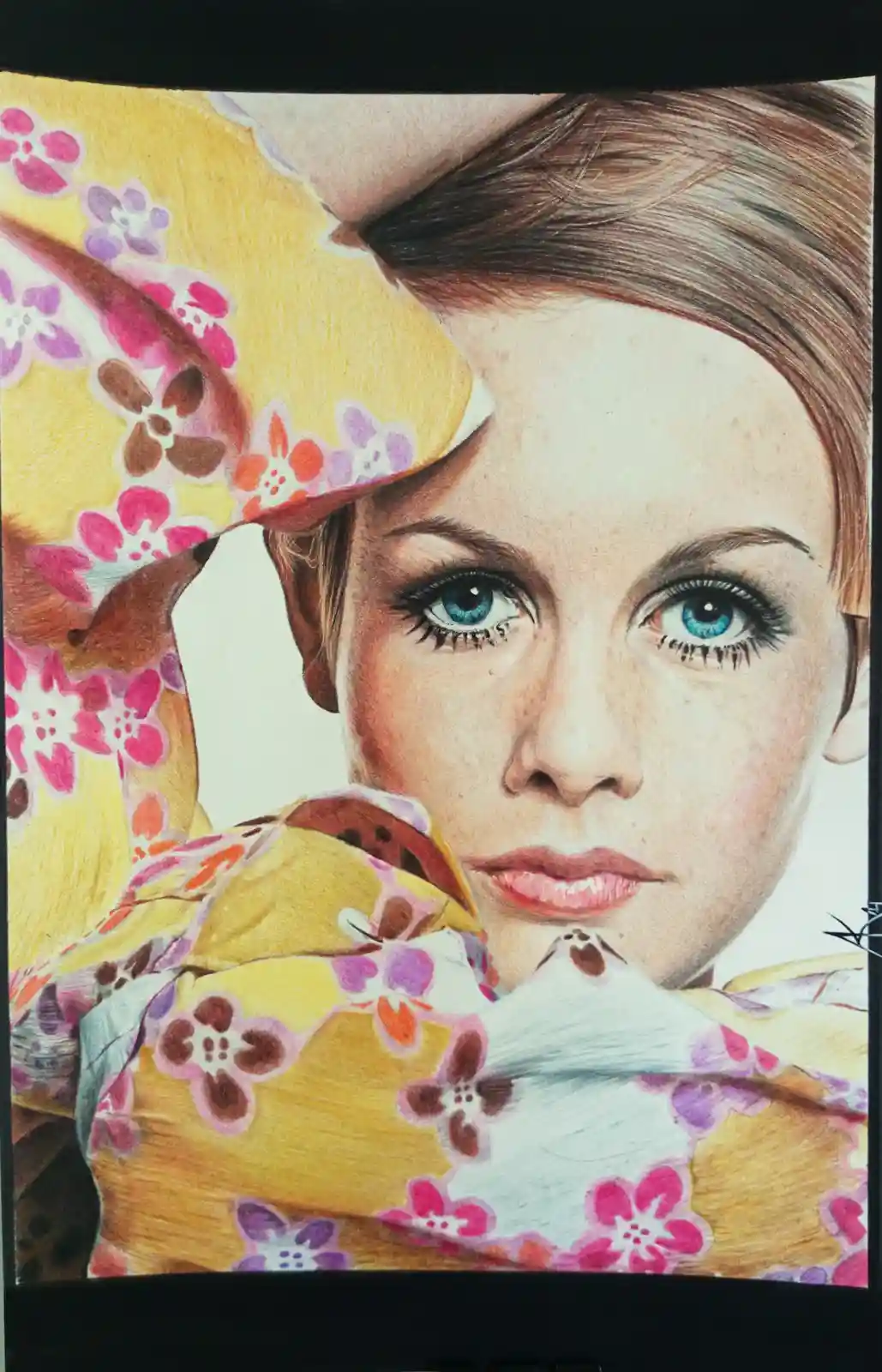 A colored pencil drawing of a woman with blue eyes and freckles, wearing a yellow floral kimono, looking directly at the…