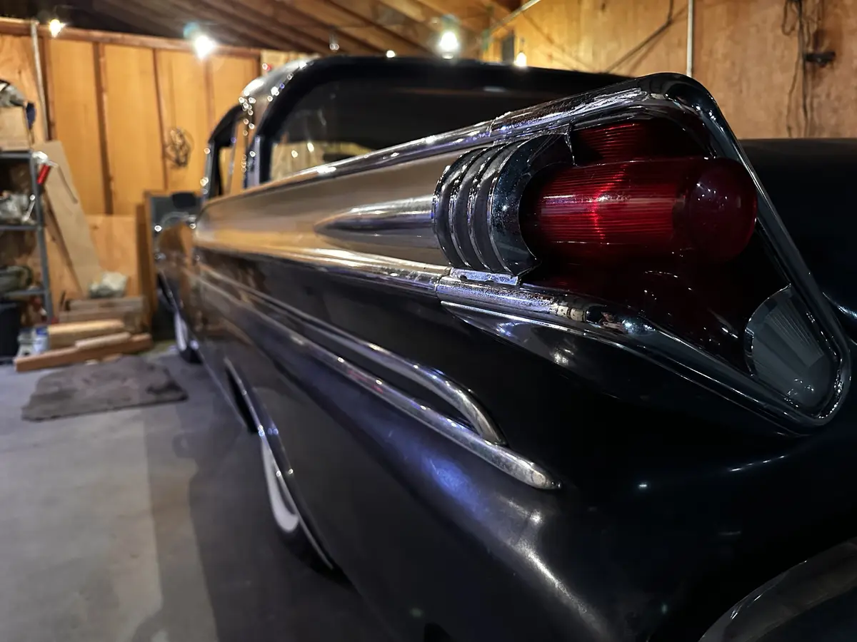 A close-up shot of the rear quarter panel and taillight of a shiny black classic car, likely from the 1950s or 60s, parked…