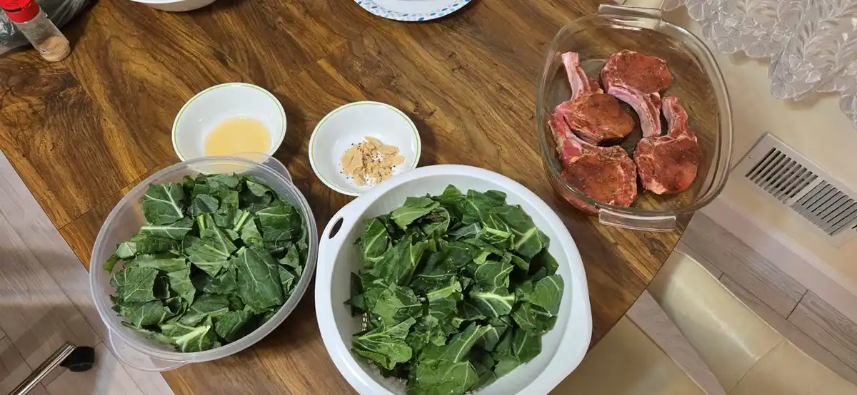 An overhead photo shows a wooden table with two large bowls filled with chopped green leafy vegetables, a small bowl of…
