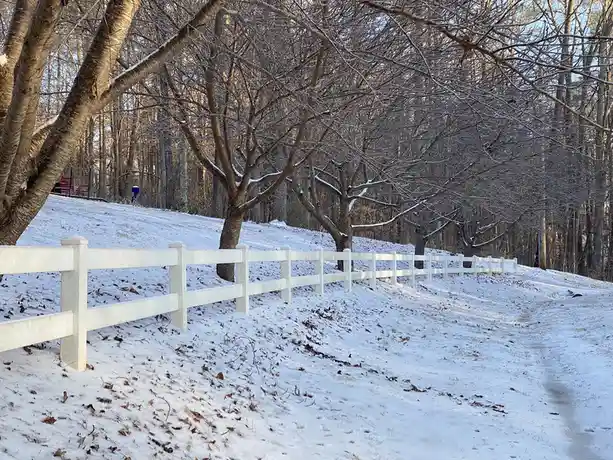 A snowy outdoor scene with a white picket fence running along a snow-covered path through bare trees. The overlaid text…