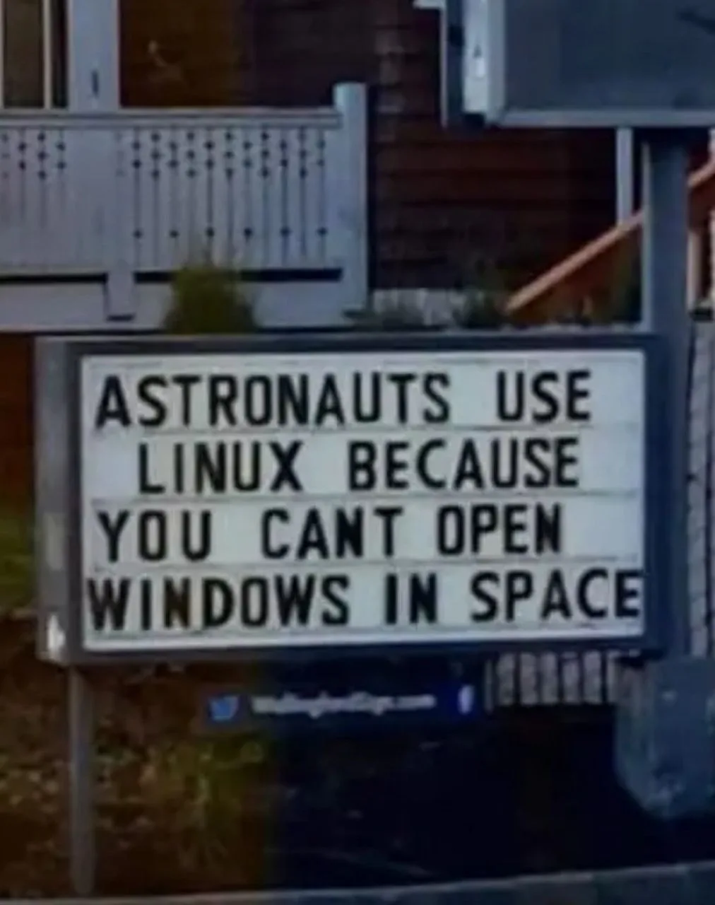 A white marquee sign with black lettering is mounted outdoors, displaying the text 'ASTRONAUTS USE LINUX BECAUSE YOU CANT…
