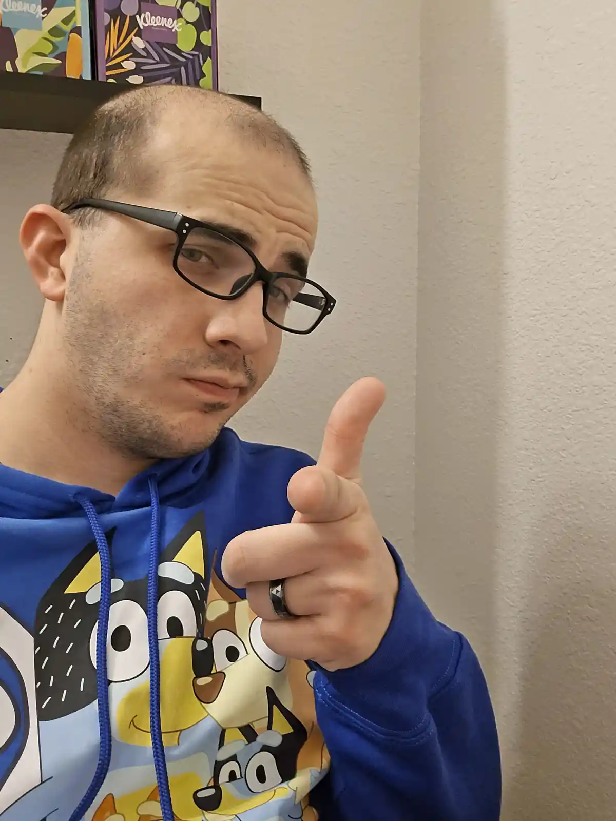 A man with glasses and a blue 'Bluey' cartoon hoodie points directly at the viewer with a skeptical, slightly smirking…