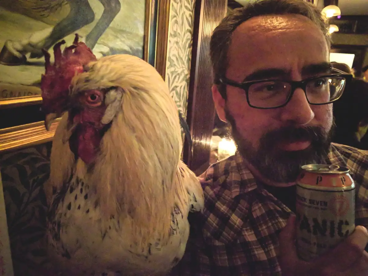 A man with glasses and a beard, wearing a plaid shirt and holding a can of 'Black Seven Panic' beer, poses with a large…
