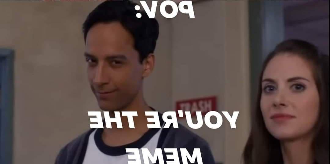 A still from a TV show shows a man with a smug, self-satisfied smirk looking slightly to his right, while a woman stands…