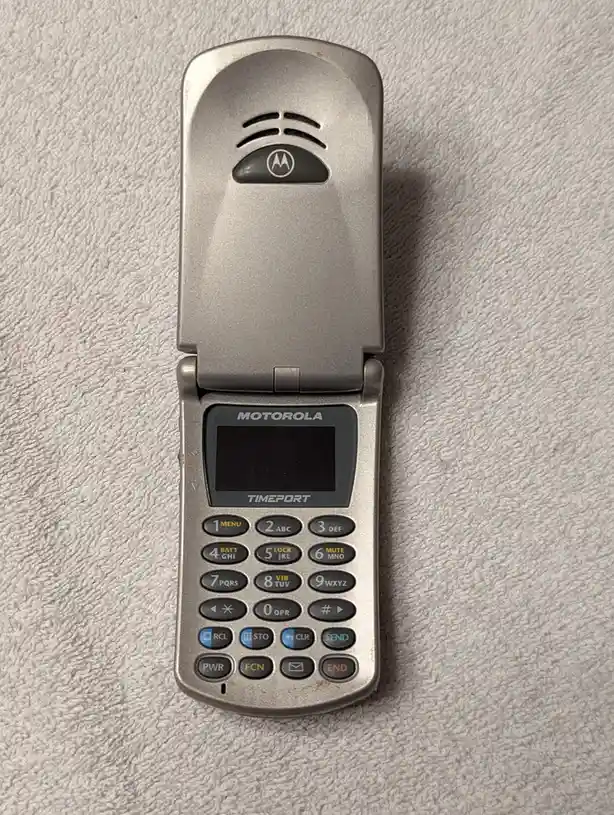 A silver Motorola Timeport flip phone, open and resting on a textured white towel, with overlaid text reading 'i'm not lazy…
