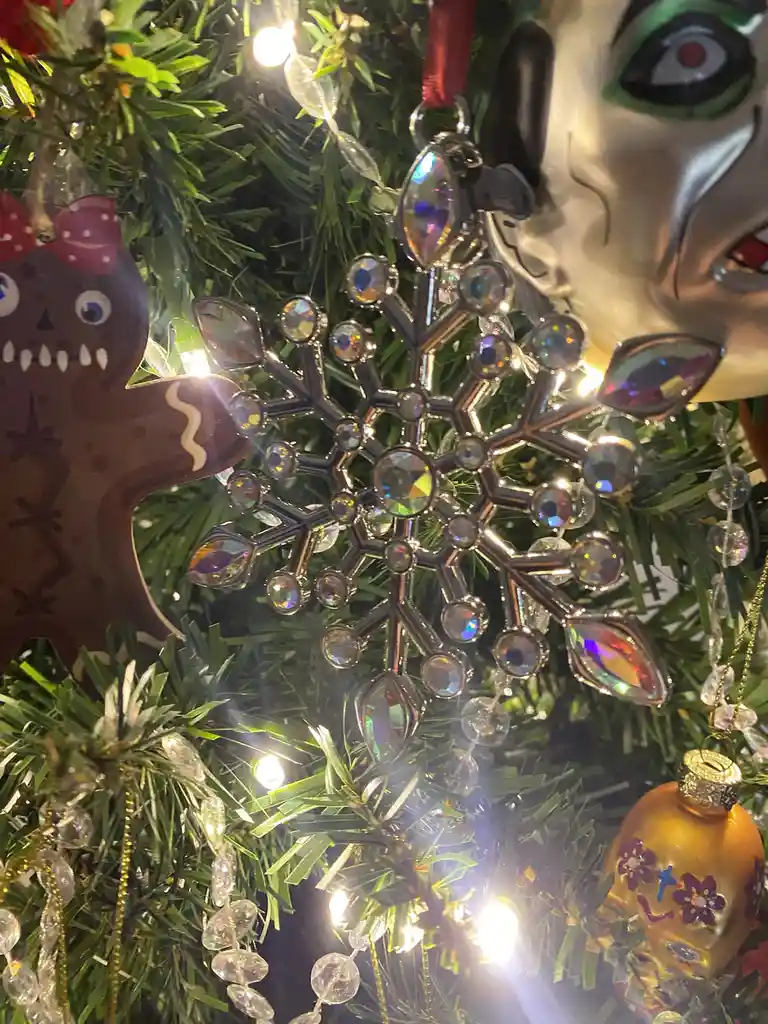 A close-up of a decorated christmas tree with a glittering snowflake ornament, a gingerbread man, and a sugar skull…