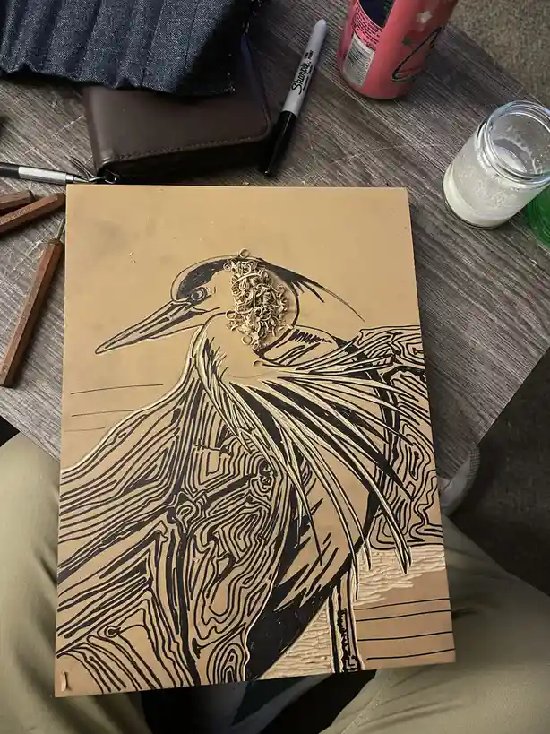 A hand-drawn illustration of a heron on brown paper, with a pile of small, tangled rubber bands placed where the bird's eyes…