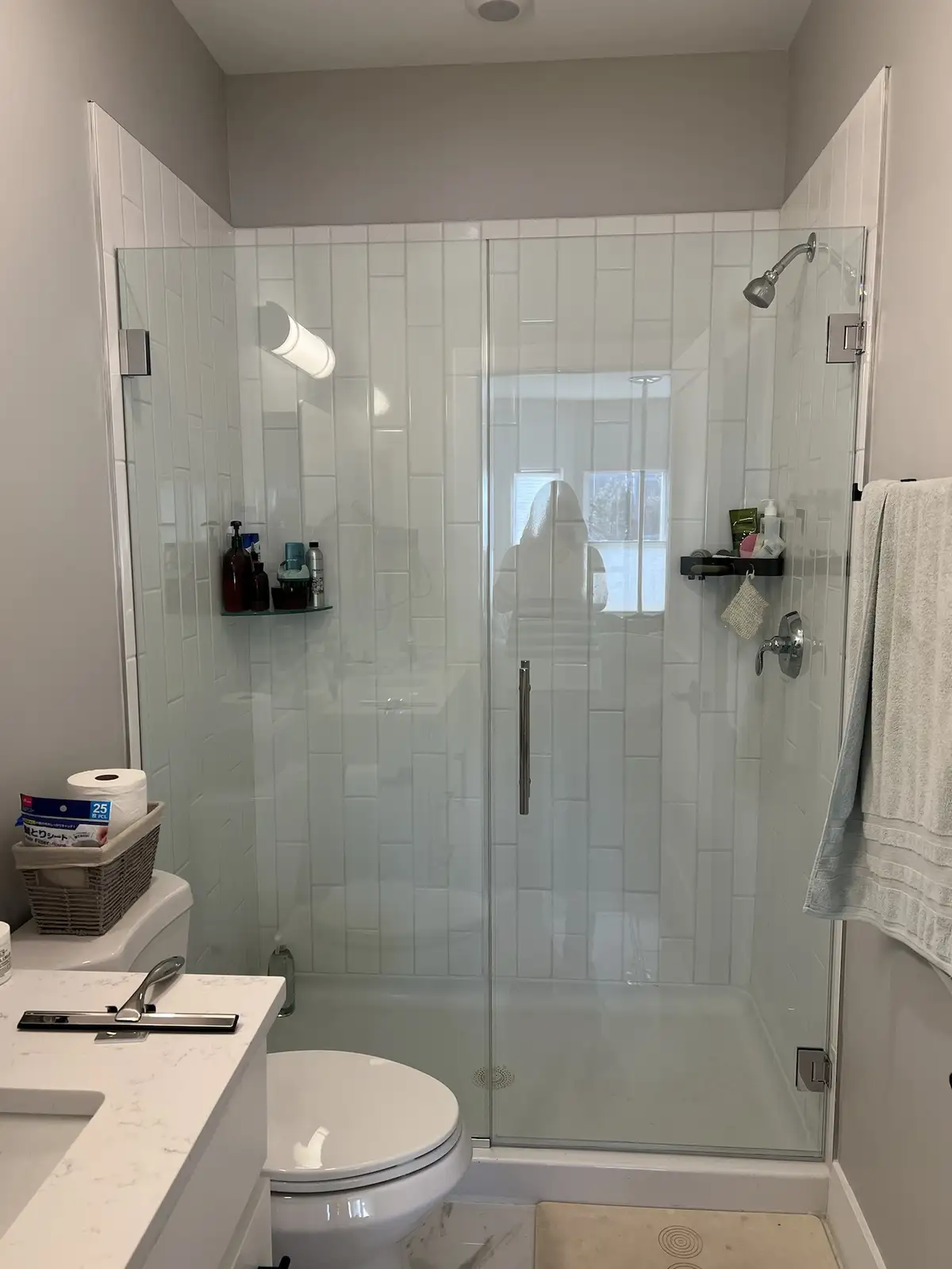 A modern bathroom with a glass shower enclosure, white subway tiles, and a toilet and sink visible. The reflection of a…