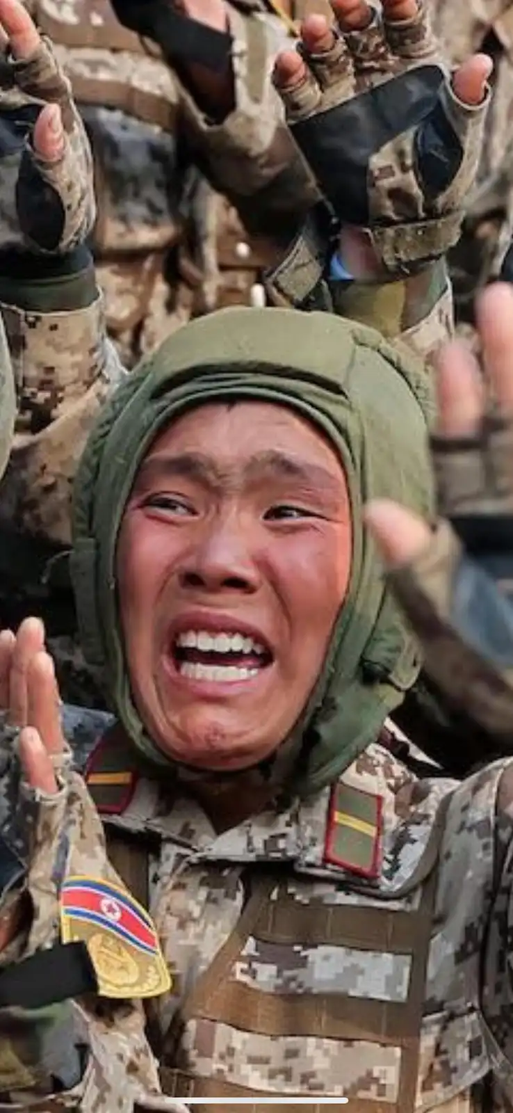 A close-up image of a North Korean soldier in camouflage uniform and green head covering, visibly crying with an open mouth…