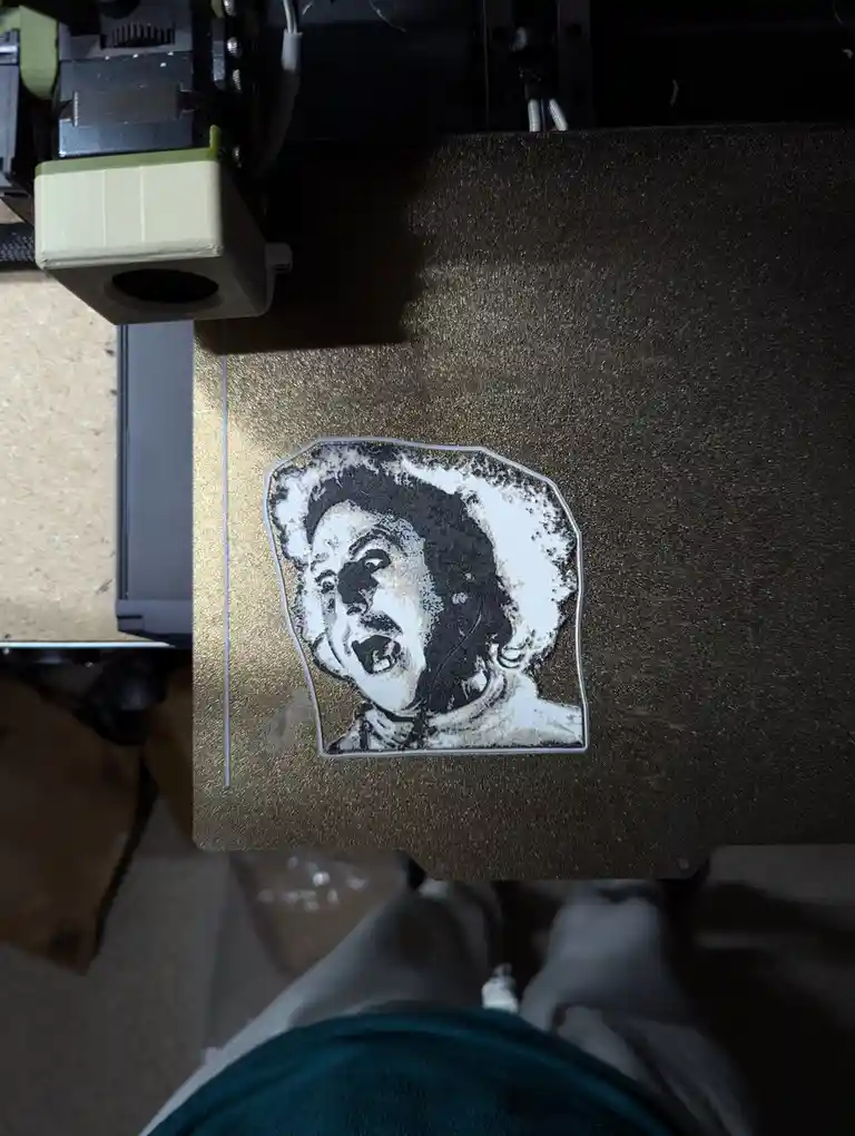 A 3D printer's print bed displays a crudely rendered black-and-white portrait of a person with an exaggerated, screaming…