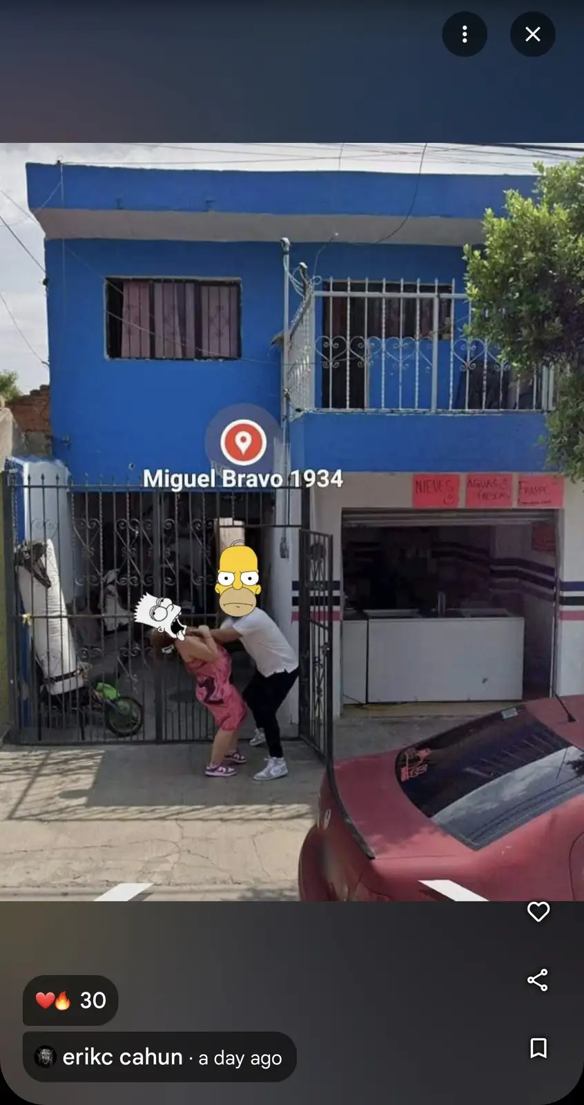 A street-level photo shows two people in front of a blue building with a metal gate; one person is holding the other by the…