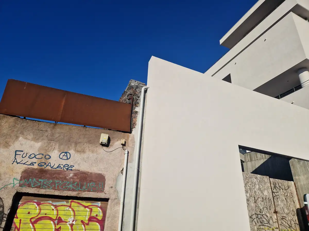 A low-angle photo shows a stark contrast between a modern, clean white building and an adjacent older, graffiti-covered wall…